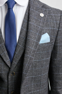 Traje a cuadros grises con corbata y pañuelo de bolsillo azules sobre un fondo gris claro.