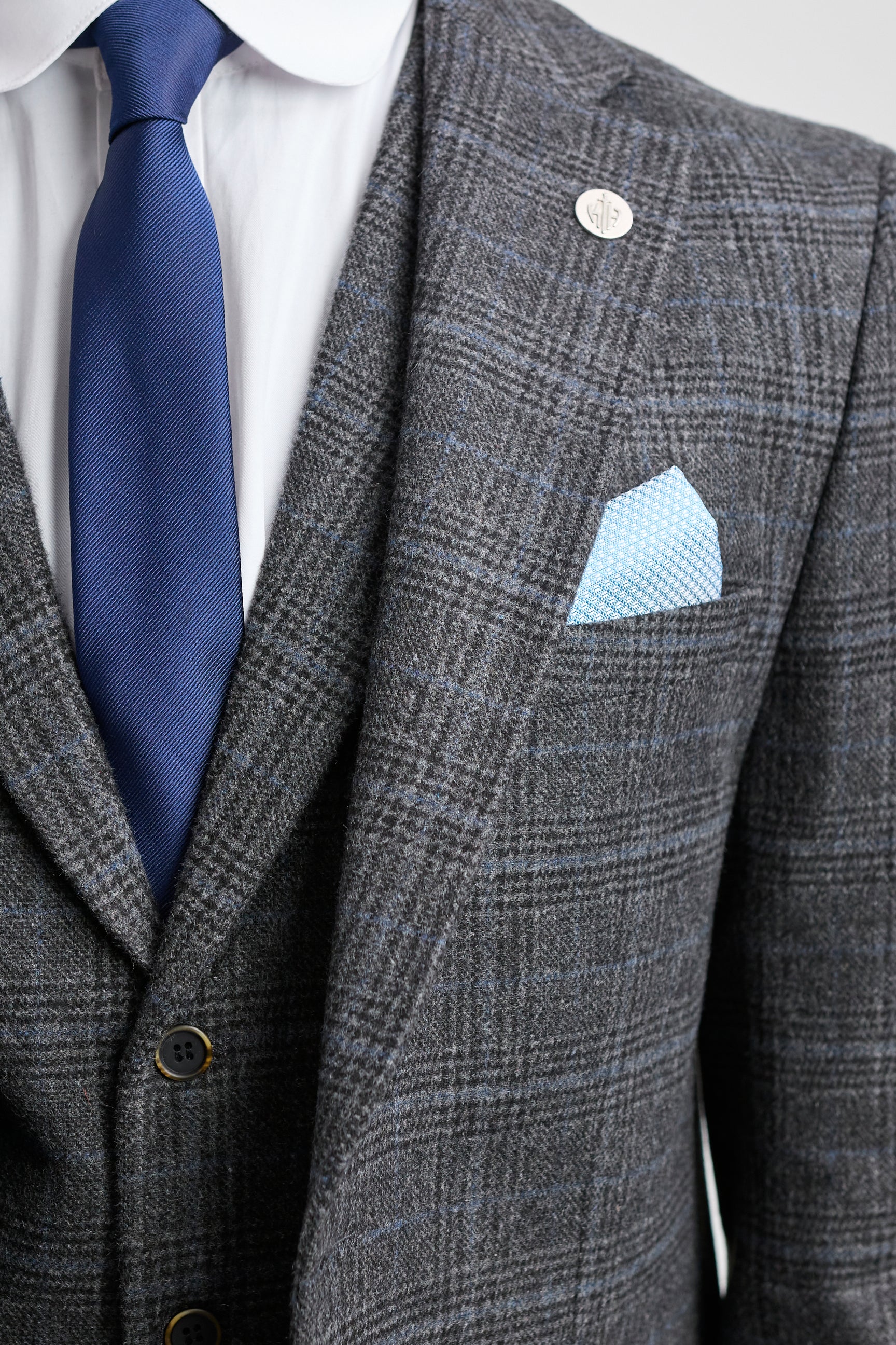 Traje a cuadros grises con corbata y pañuelo de bolsillo azules sobre un fondo gris claro.
