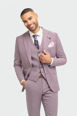 Hombre con traje lila claro, camisa blanca y corbata estampada sobre fondo gris claro.