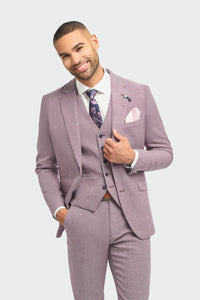 Hombre con traje lila claro, camisa blanca y corbata estampada sobre fondo gris claro.