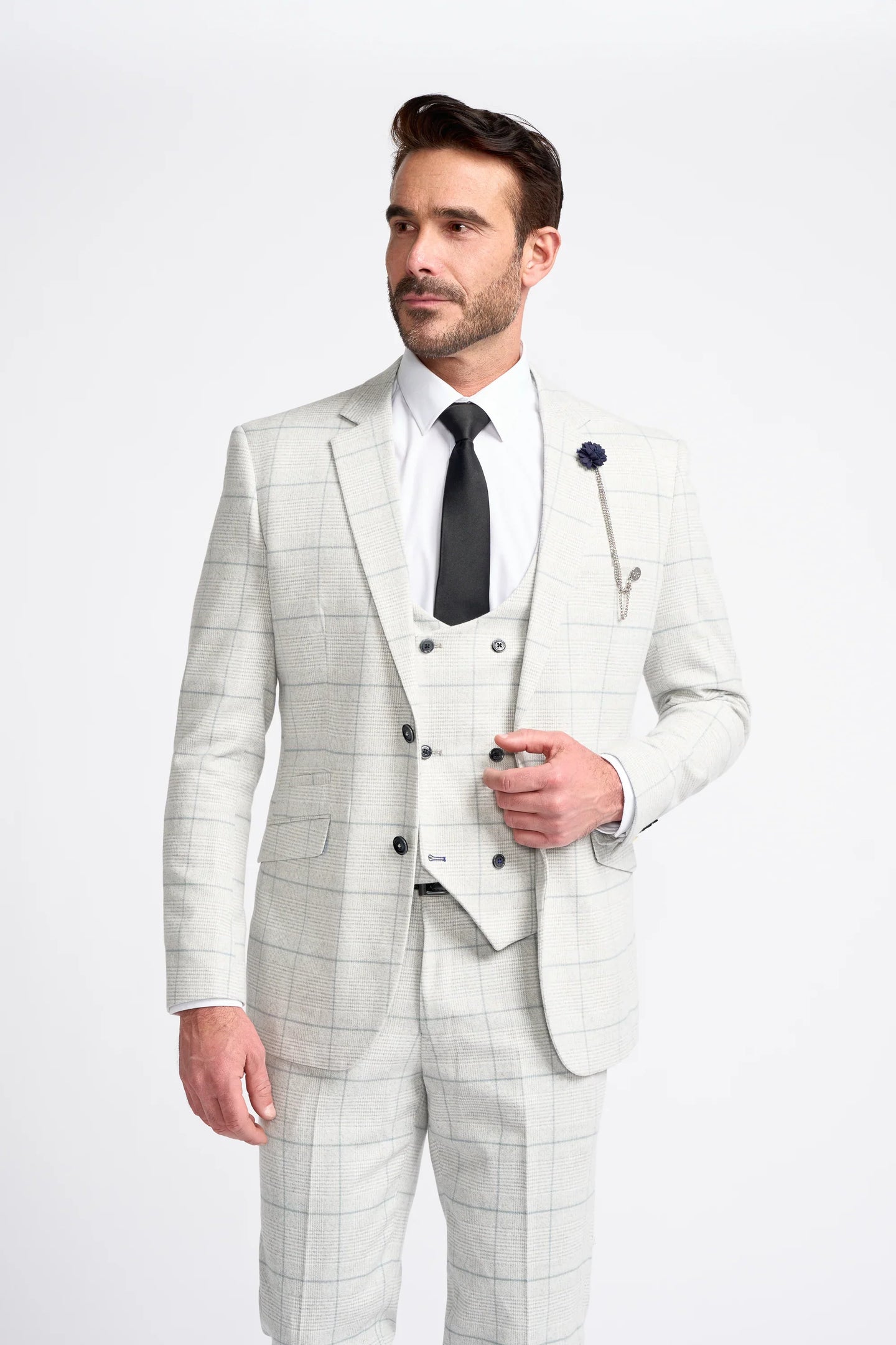 Hombre con traje a cuadros gris claro, camisa blanca y corbata negra sobre fondo blanco.