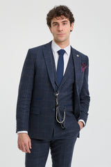 Hombre con traje a cuadros azul, camisa blanca y corbata azul sobre fondo gris claro.