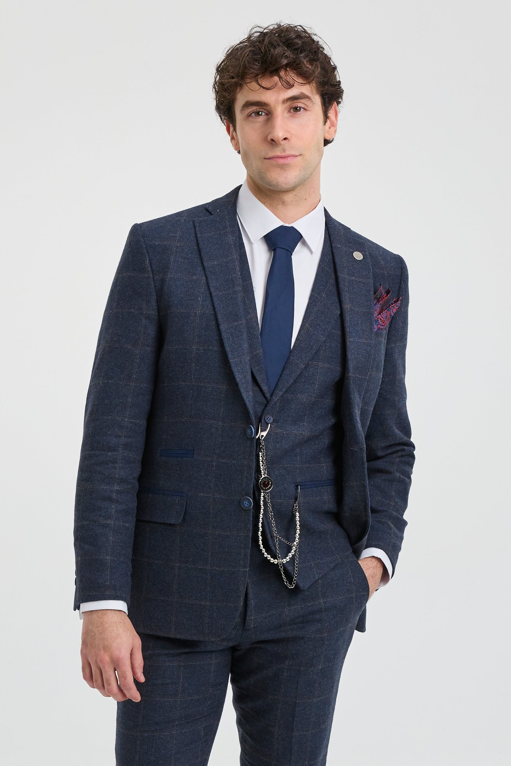 Hombre con traje a cuadros azul, camisa blanca y corbata azul sobre fondo gris claro.
