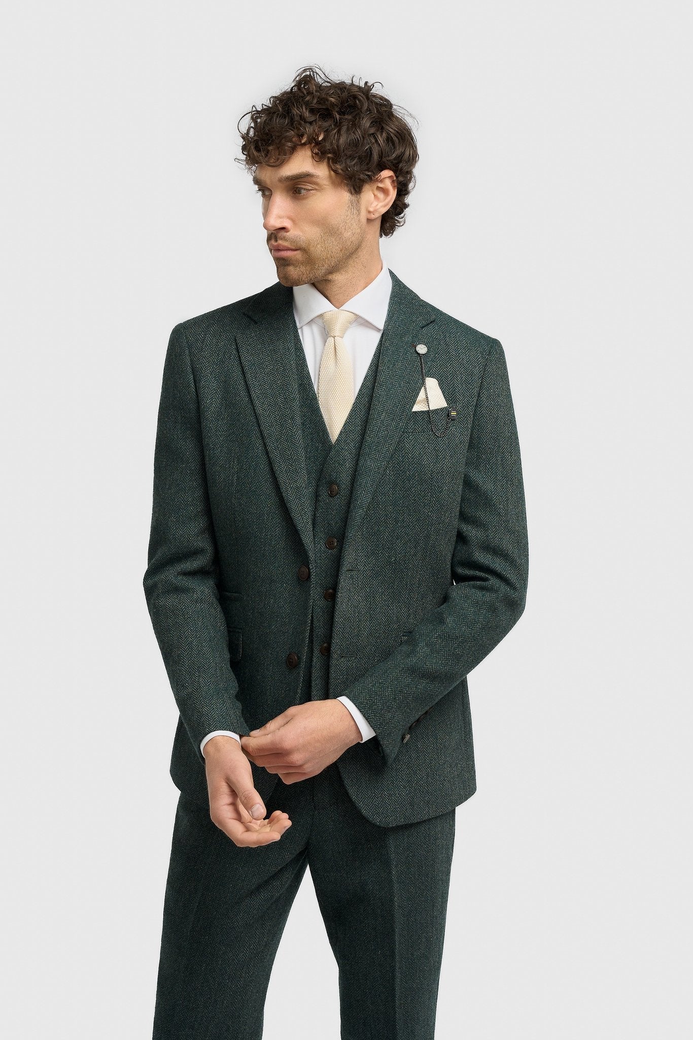 Hombre con traje verde, camisa blanca y corbata sobre un fondo gris claro.