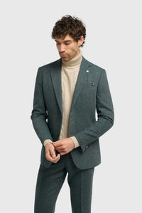 Hombre con traje verde y jersey de cuello alto beige sobre fondo blanco.
