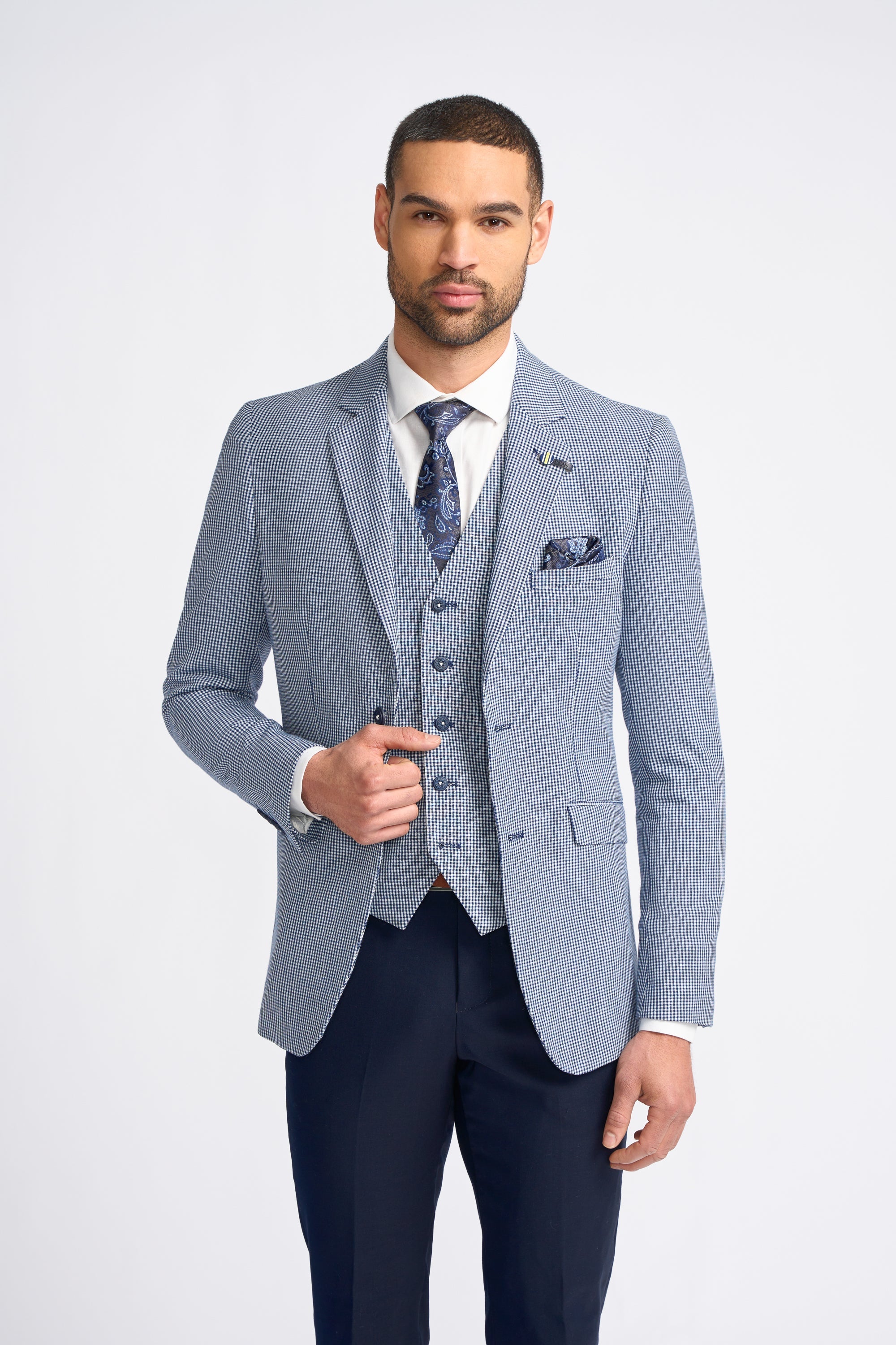 Hombre con traje a cuadros azul claro, camisa blanca y corbata estampada sobre fondo blanco.