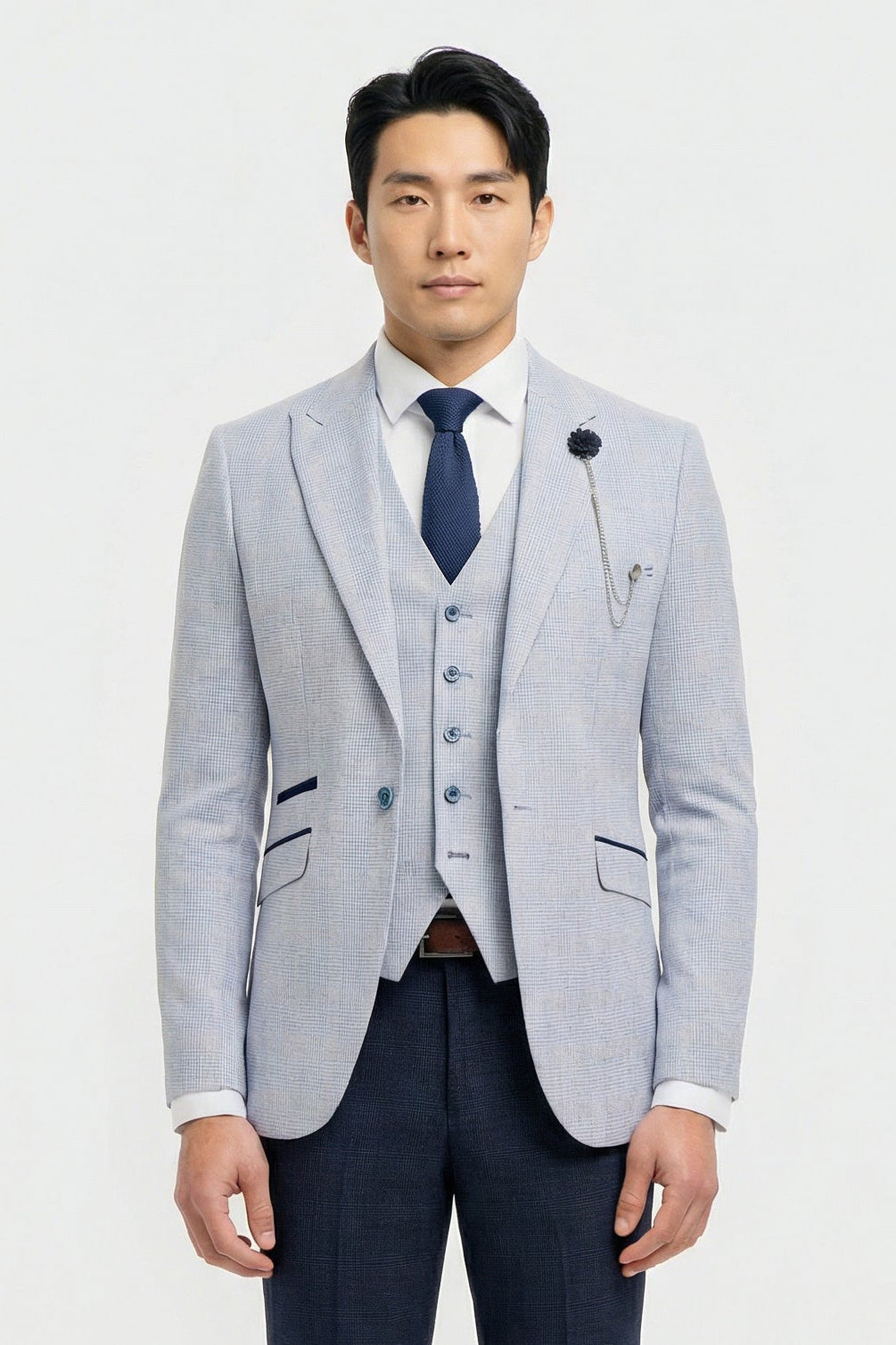 Hombre con chaqueta gris claro, chaleco azul marino y corbata azul oscuro sobre fondo blanco.