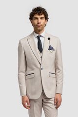 Hombre con traje beige, camisa blanca y zapatos marrones sobre un fondo gris claro.