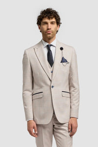 Hombre con traje beige, camisa blanca y zapatos marrones sobre un fondo gris claro.