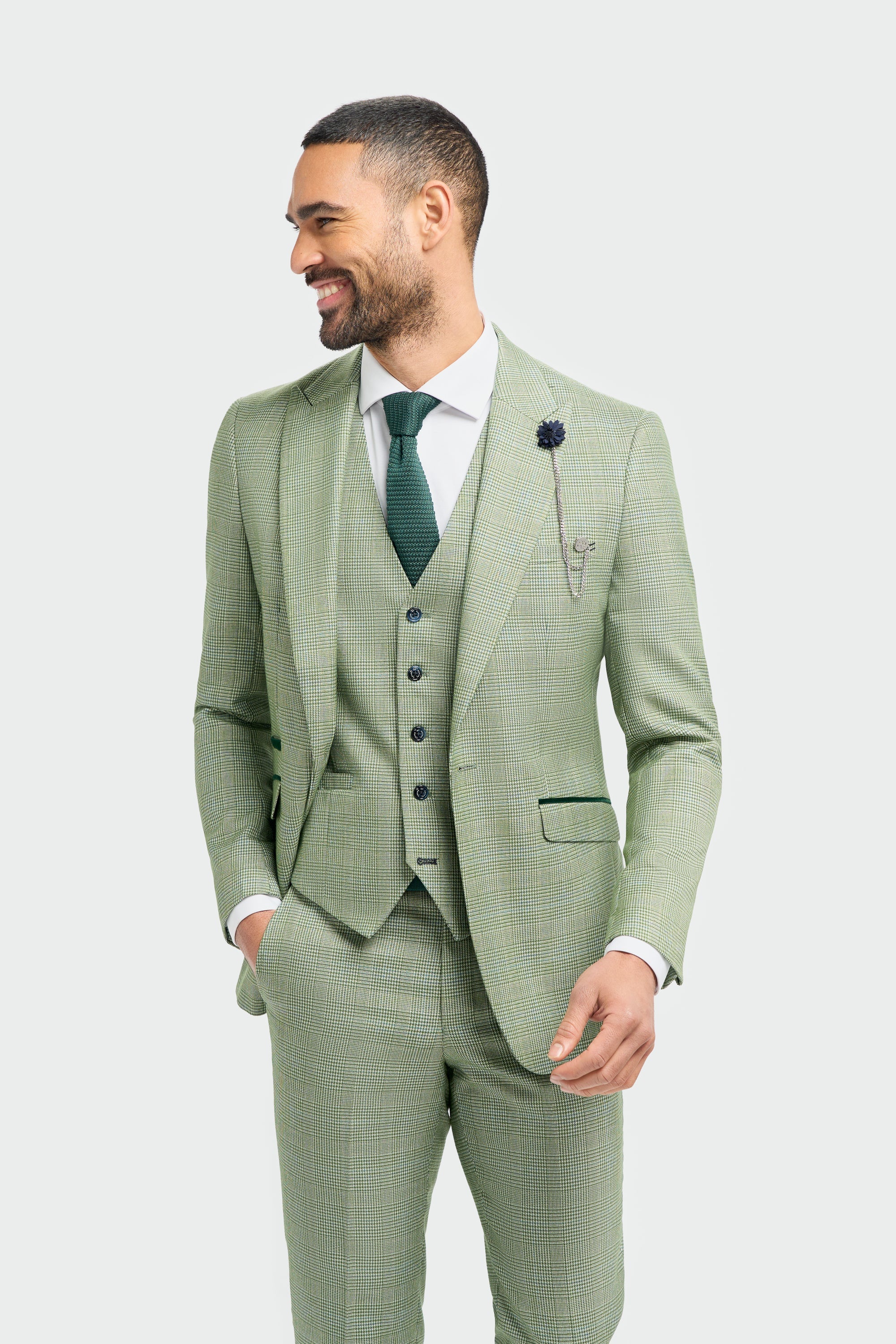 Hombre con traje a cuadros verde claro, camisa blanca y corbata verde sobre fondo blanco.