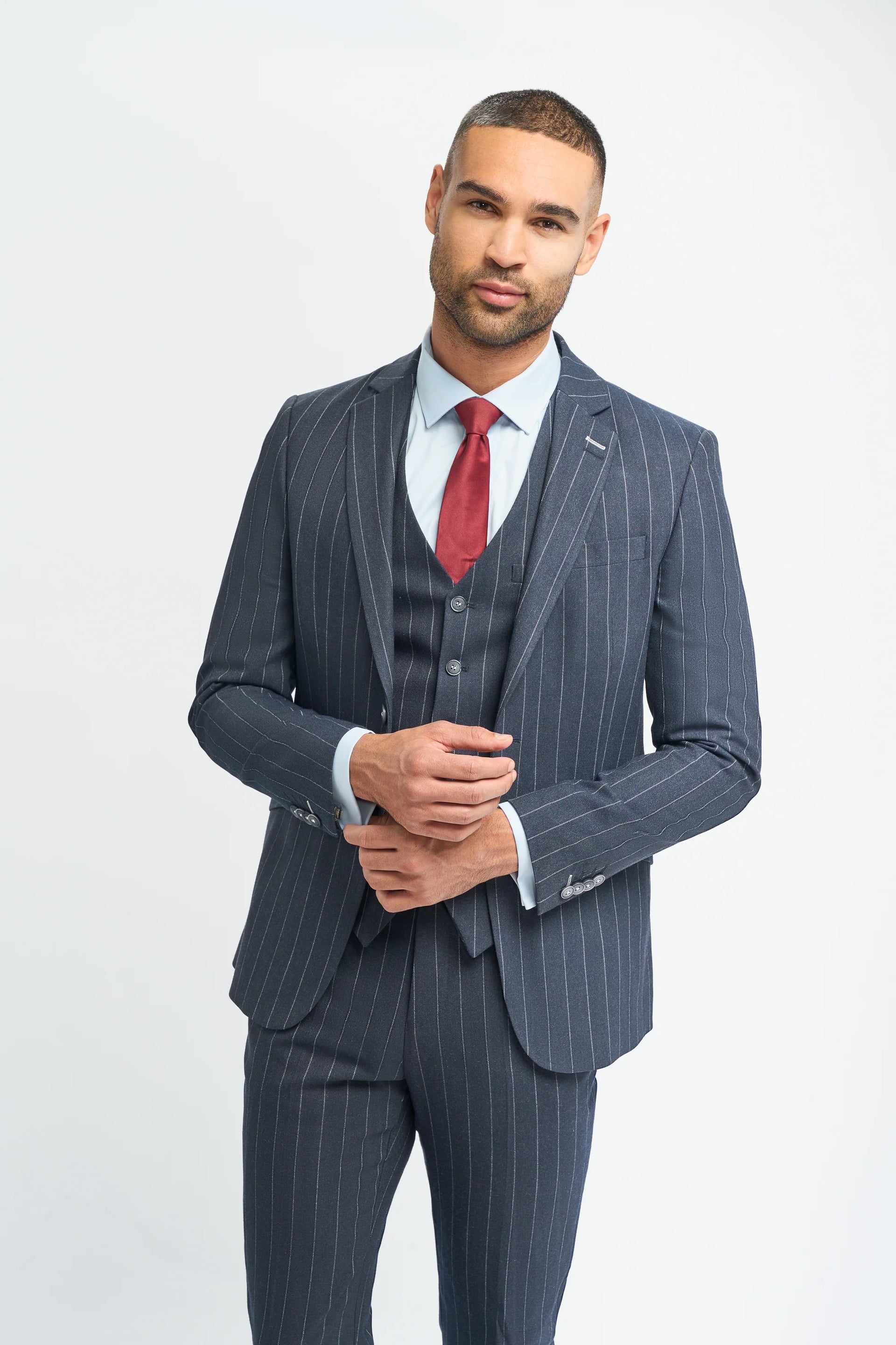 Hombre con traje gris de raya diplomática y corbata roja sobre fondo blanco.