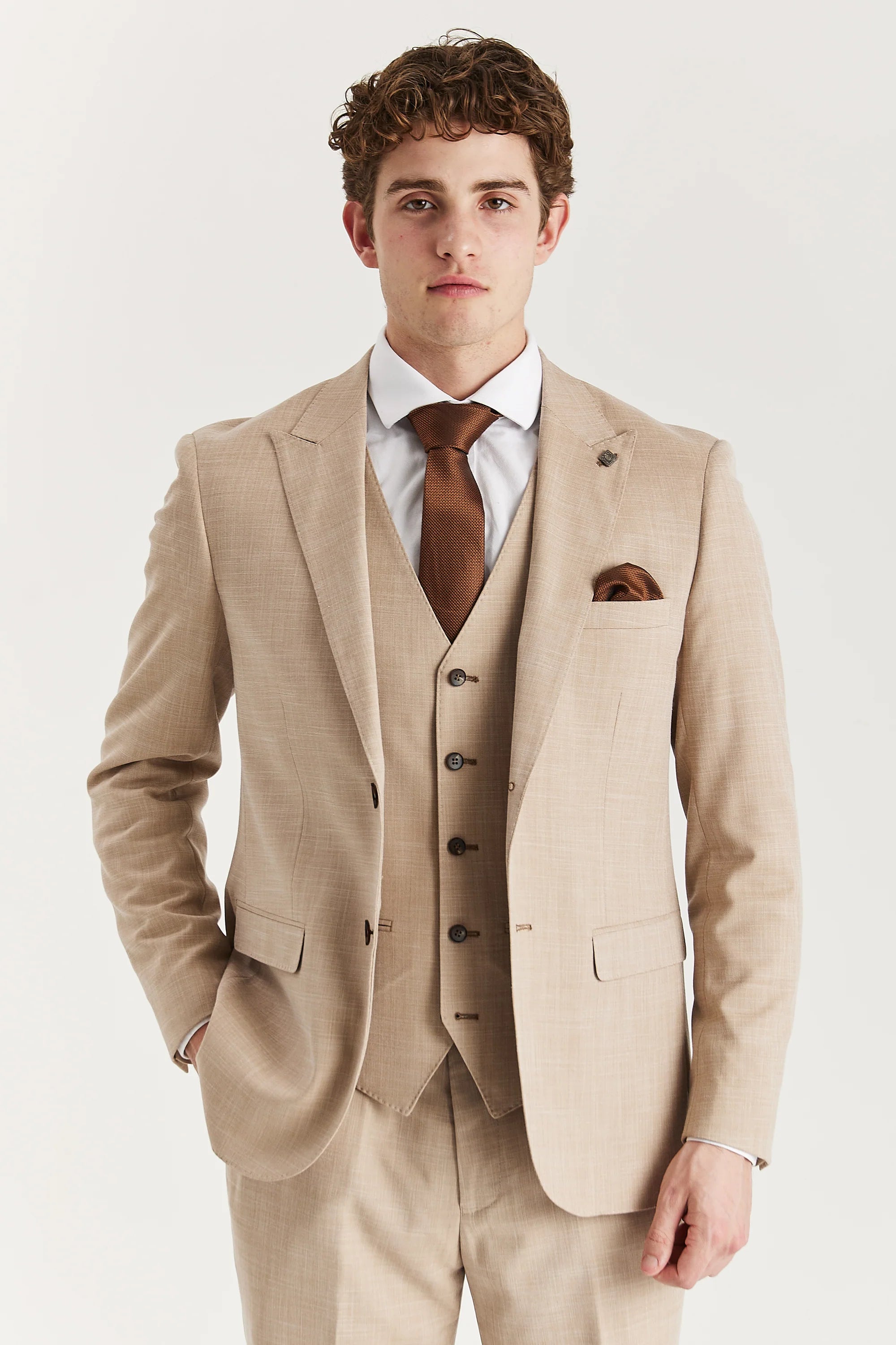 Hombre con traje beige y corbata marrón sobre fondo blanco