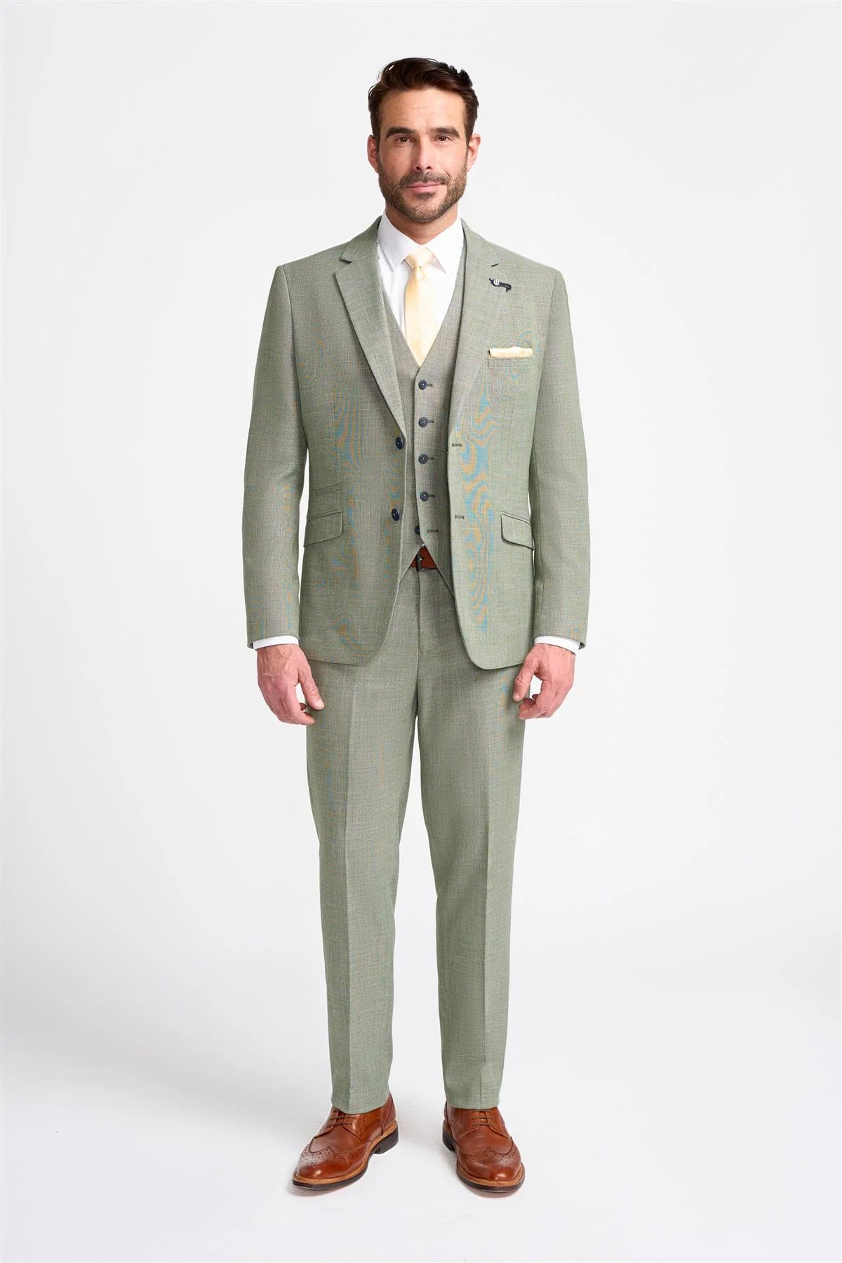 Hombre con traje gris claro, camisa blanca y zapatos marrones sobre fondo blanco.