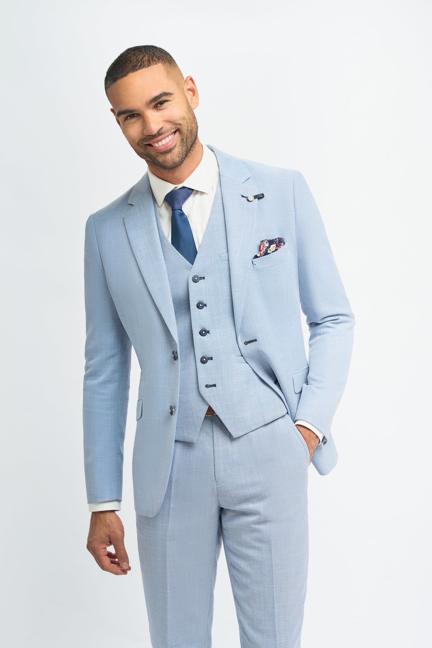 Hombre con traje azul claro, camisa blanca y corbata azul sobre fondo liso.