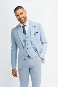 Hombre con traje azul claro, camisa blanca y corbata azul sobre fondo liso.