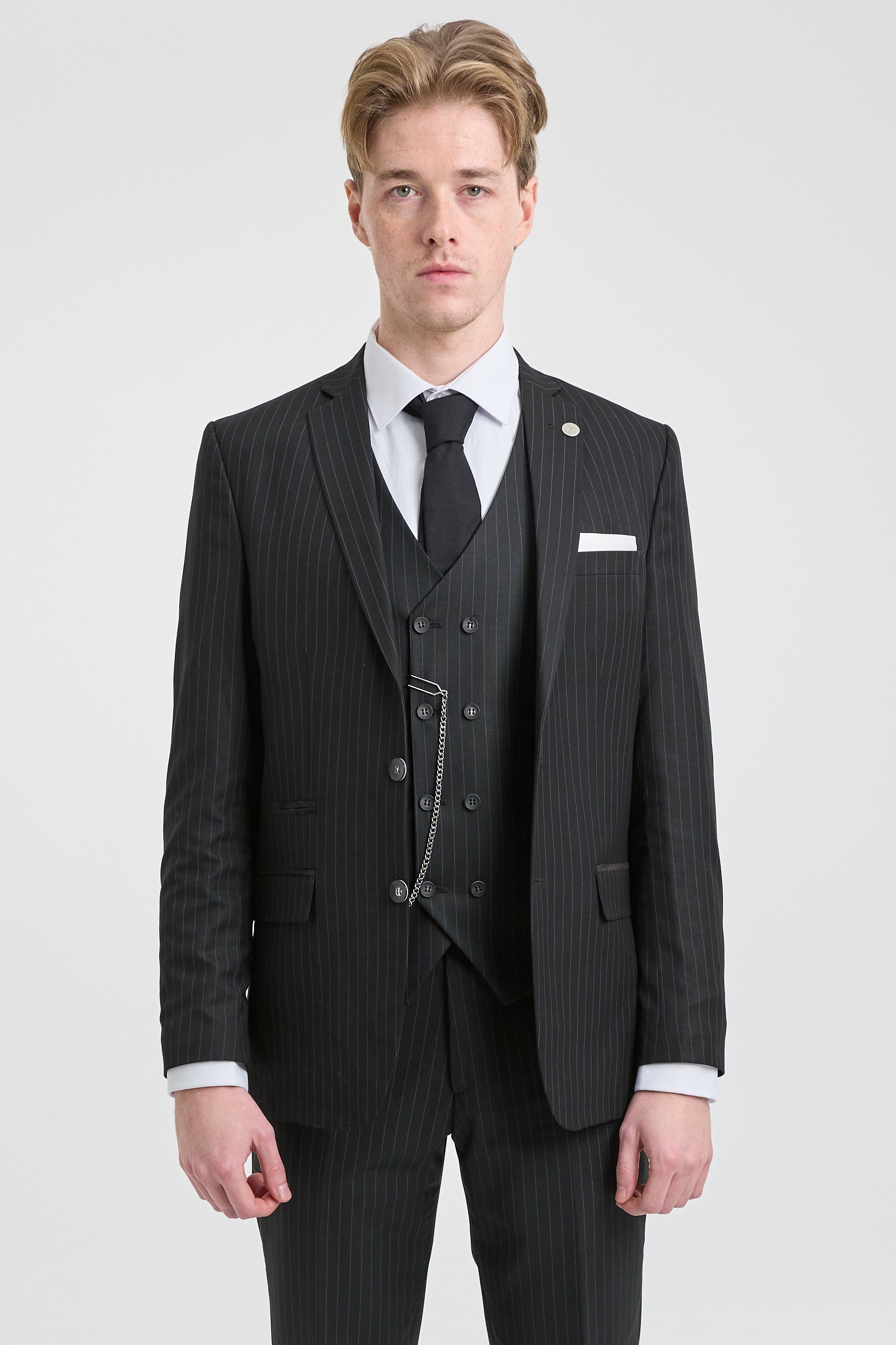 Hombre con traje negro de raya diplomática, camisa blanca y corbata negra sobre un fondo gris claro.